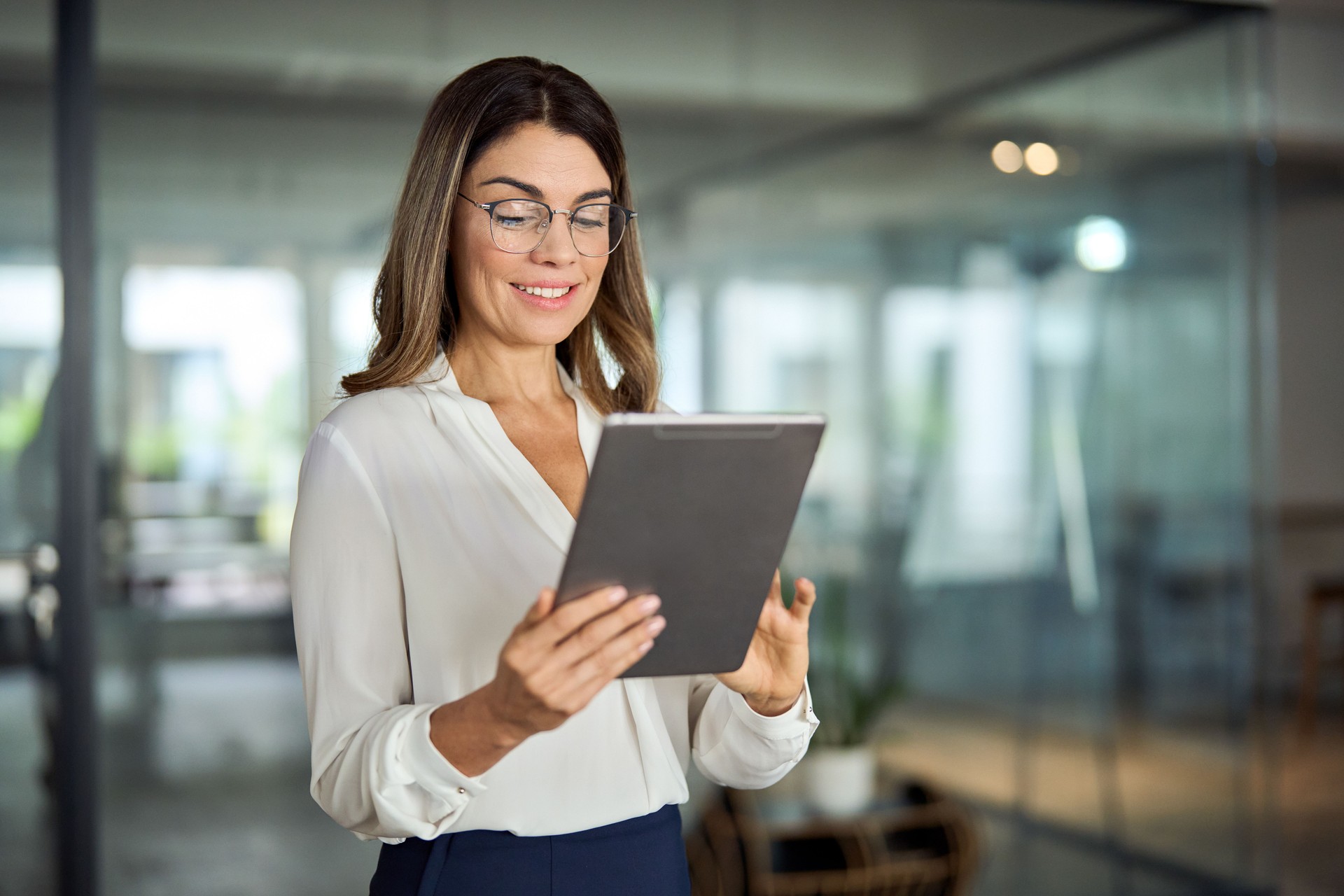 Smiling mid aged professional business woman holding tablet in office.